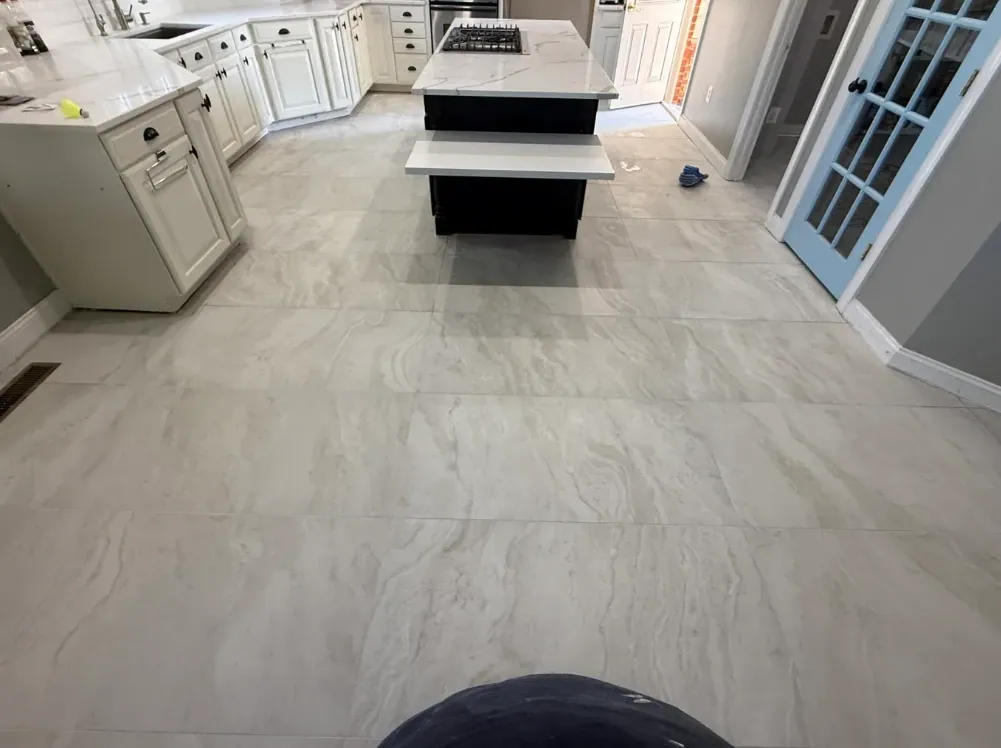 Gray veined tile floor between white kitchen cabinets, a black island, and a blue glass-paneled door.