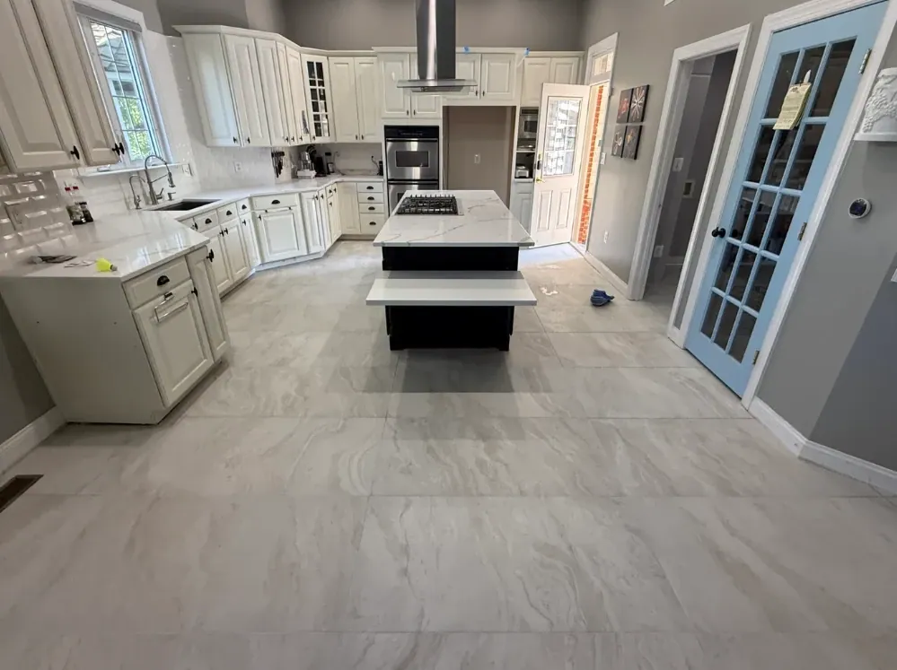 Wide kitchen view with white cabinets, a black island, a blue glass-paneled door, and gray veined tile flooring.