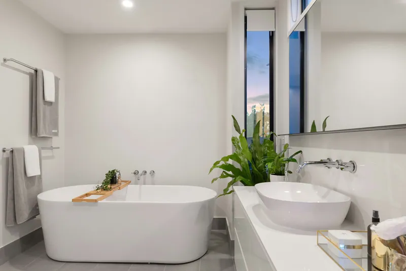 Freestanding white tub and white vessel sink beside a narrow turquoise-glazed window in a bright bathroom.